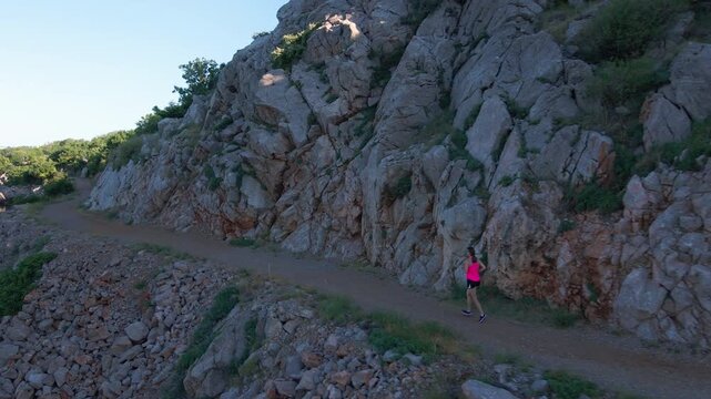 Woman running on mountain trail beside rocky cliff