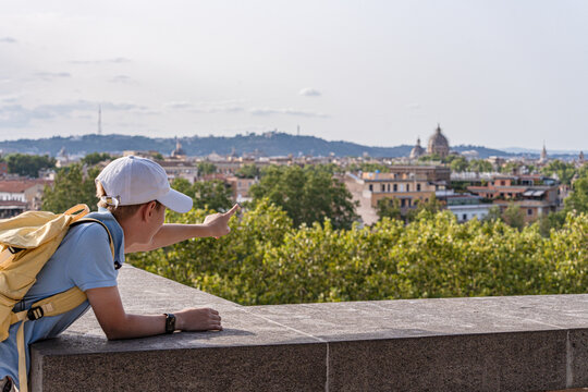 Side view of a teenage boy leaning on a wall pointing at the distant cityscape, Parco Savello (Orange Trees Garden), Rome, Lazio, Italy