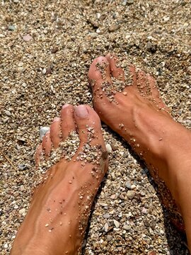 Close-up of a woman's tanned feet on a pebble beach in summer