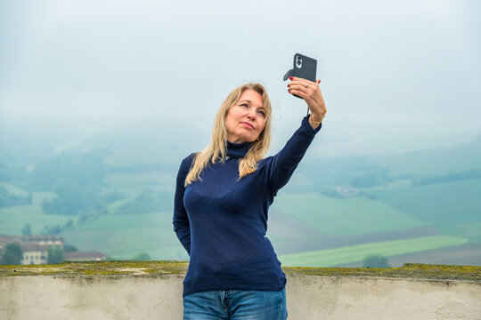 Portrait of a woman standing at an observation point taking a selfie in front of the Langhe Hills on a misty day, Piedmont, Italy