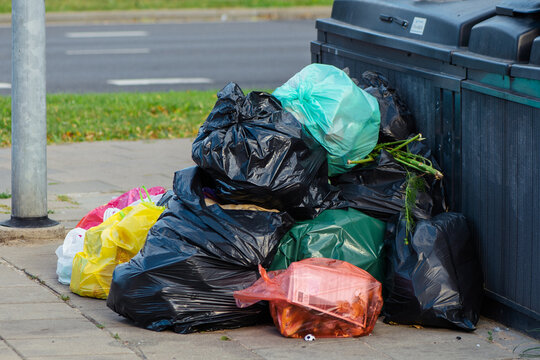 Pile of assorted household garbage bags left next to public waste containers on a sidewalk