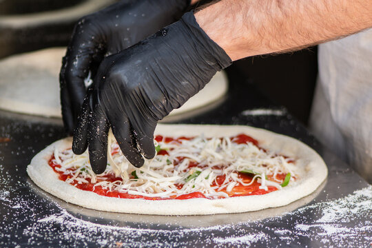 Pizza maker with black gloves preparing a Neapolitan-style pizza on a floured metal counter