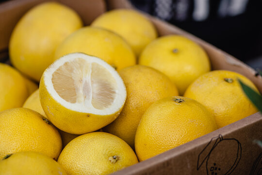 Box of fresh Pomelo or Sweetie citrus fruit, featuring one fruit cut in half, packed inside a cardboard box at a fruit and vegetables market
