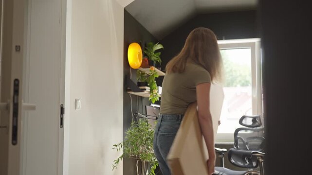 Woman carrying shelving box into home office for furniture assembly
