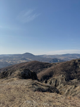 Mountain landscape with ridges, bare trees, and distant blue horizon.