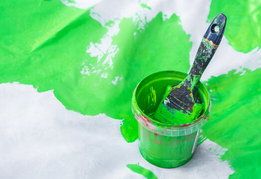 Small bucket filled with vibrant green paint and a paintbrush resting inside, set against a white surface with green paint splatters