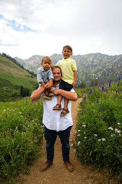 Man standing on a footpath in an alpine landscape with his two young sons sitting on his shoulders, Albion Basin Meadow, Albion Basin, Little Cottonwood Canyon, Utah, USA