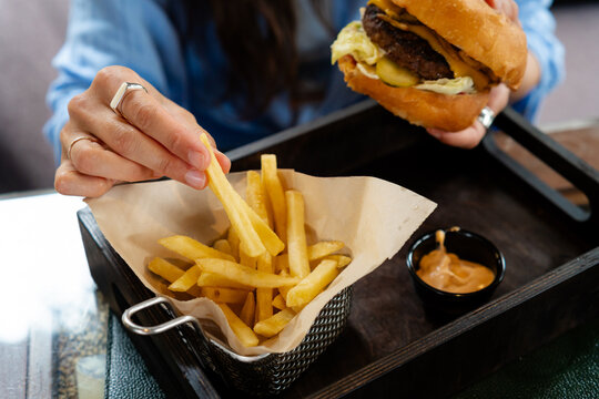Close-up of a woman sitting at a table in a cafe eating a hamburger and french fries