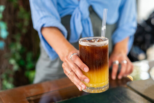 Close-up of a young Woman standing at a table outdoors drinking an Iced Bumble Coffee drink on a summer day