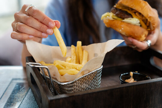 Close-up of a woman sitting at a table in a cafe eating a hamburger and french fries