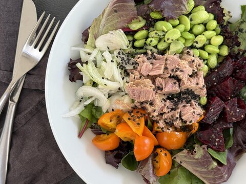 Close-up overhead view of a salad with tuna, edamame beans, beetroot, cherry tomatoes, spring onion and black sesame seeds on a table with cutlery