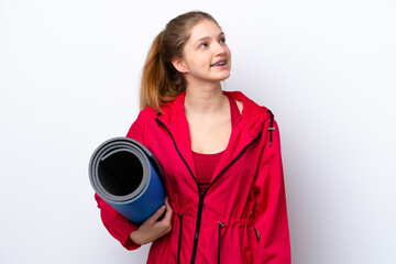 Teenager girl going to yoga classes while holding a mat isolated on white bakcground thinking an idea while looking up © luismolinero