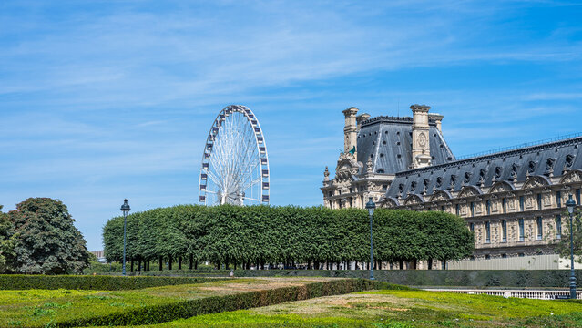 The image shows the garden of Tuileries with a view of the Louvre Museum and the Roue de Paris Ferris wheel in Paris, France