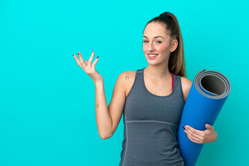 Young sport caucasian woman going to yoga classes while holding a mat isolated on blue background extending hands to the side for inviting to come © luismolinero
