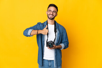 Naklejka premium Young photographer girl isolated on yellow background giving a thumbs up gesture
