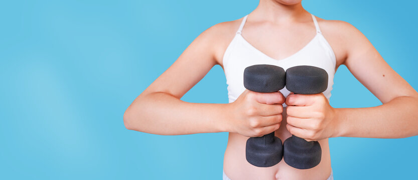 Woman holding small black dumbbells near chest indoors, home fitness training, healthy lifestyle.