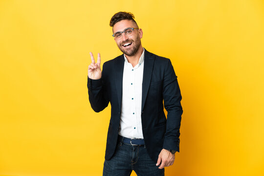 Businessman over isolated yellow background smiling and showing victory sign