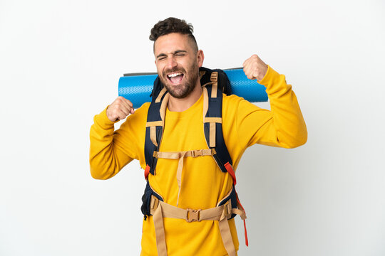 Young mountaineer man with a big backpack over isolated background celebrating a victory