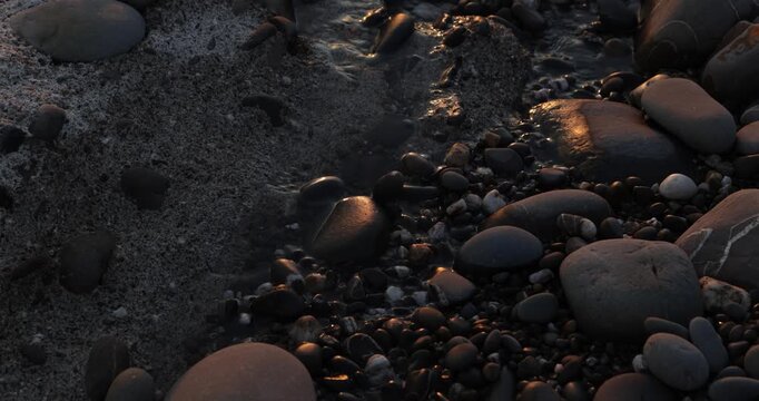 Zen pebble stones on the foreshore of small trickling beach stream lit by the golden light of the setting sun during a peaceful sunset golden hour.  4K natural landscape  
