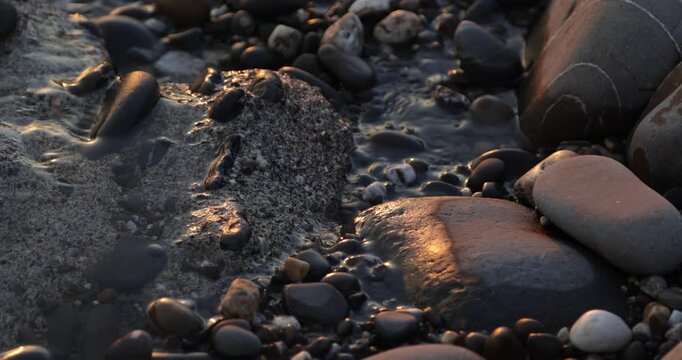Zen pebble stones on the foreshore of small trickling beach stream lit by the golden light of the setting sun during a peaceful sunset golden hour.  4K natural landscape  