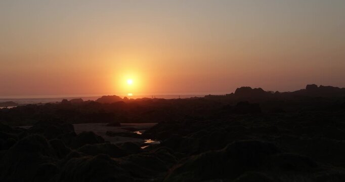 beautiful static shot of a stunning sunset over a Cornish beach in Cornwall UK of a golden orange sun setting over glistening rockpools on a rocky shingle beach 4K