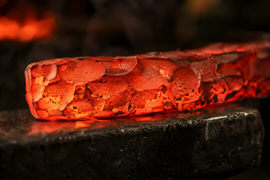 Glowing red hot forged steel workpiece with hammer marks on dark iron anvil macro close up industrial blacksmith metalwork background