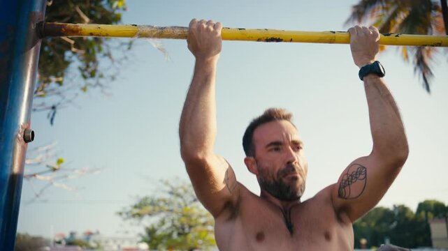 Athletic man with tattoos doing a pull-up workout on a horizontal bar at an outdoor gym
