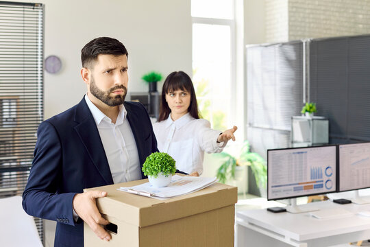 Employee faces manager after being fired. Upset employee carries a box as the manager points to the office exit, showing conflict, dismissal and unemployment. Layoff and office conflict theme.