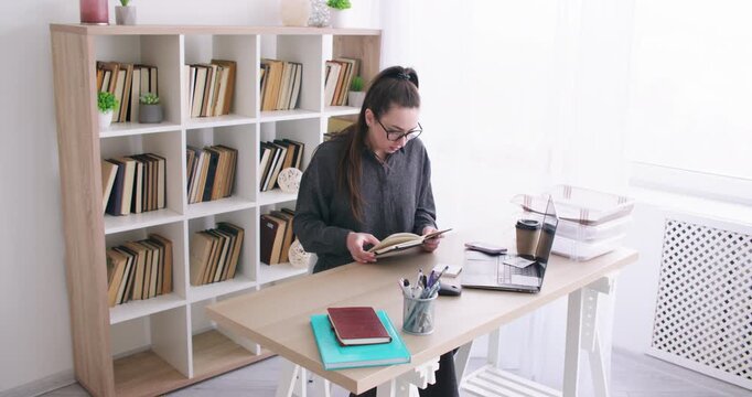 Office routine. Low productivity. Bored female employee at desk with laptop notebook analyzing business paperwork at modern workspace.
