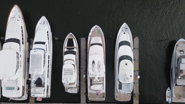 Smooth aerial drone shot flying sideways along a pier with a row of luxury yachts moored at a marina in Florida, passing directly over the boats.