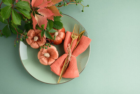 Autumn harvest table setting with decorative pumpkins and golden cutlery on a pastel plate