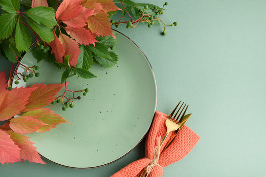 Autumn table setting with plate cutlery napkin and colorful leaves against plain background