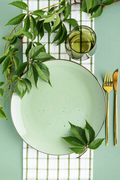 Green plate with golden cutlery and vine leaves on checkered cloth composition for healthy lifestyle meal promotion
