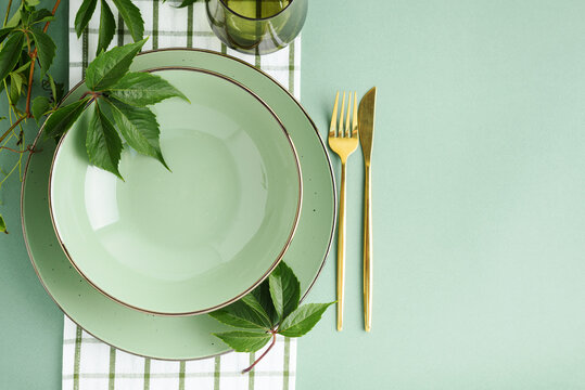 Elegant table setting with green plates and golden cutlery and fresh green leaves for a healthy lifestyle and dining.