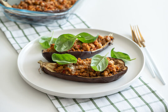 Two baked eggplant halves filled with savory mixture and garnished with fresh basil leaves on a white plate with golden forks