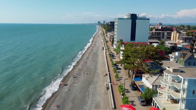 A beautiful aerial view along the Black Sea coast in Kobuleti, Georgia, showing Pebble Beach with tourists, the promenade, and modern city buildings under clear blue skies