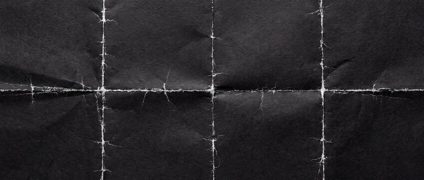 Black paper texture with worn white fold lines forming a grid pattern on dark background with paper surface prominent distressed material abstract document cracked