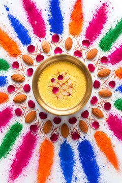 Brass bowl of thandai surrounded by almonds rose petals and holi colors