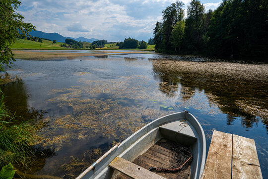 Ruderboot an einem h&ouml;lzernen Steg am Ufer eines ruhigen Sees.