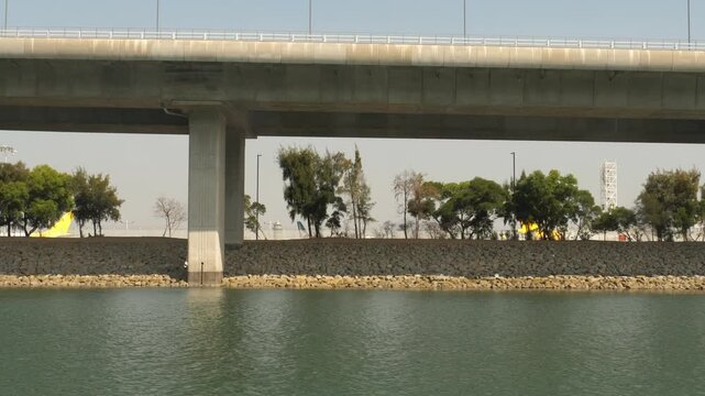 Hong Kong Zhuhai Macao Bridge viaduct over sea water near airport green shoreline with airplane tails visible in background on sunny day, tracking camera movement