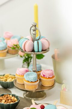 Sweet Delights Display: A tiered stand laden with pastel-colored cupcakes and macarons, accompanied by bowls of nuts and a solitary candle, creates an inviting dessert table setup for a celebration.