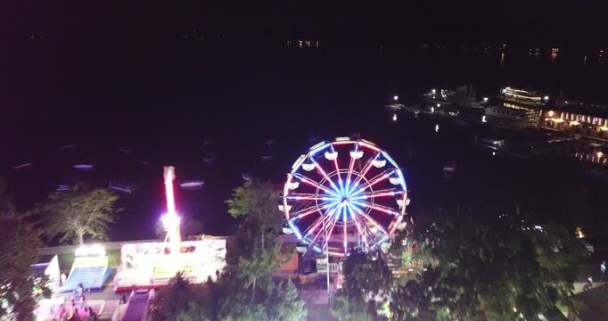 Aerial drone video flying towards a ferris wheel and over other amusement rides with lots of lights at a carnival in Lake Geneva, Wisconsin.