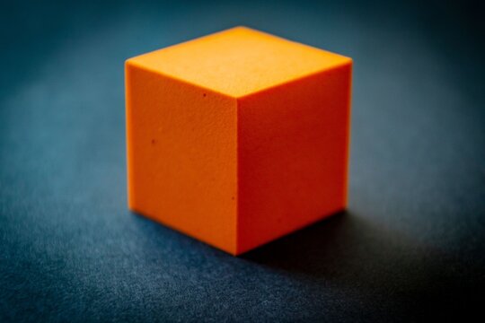 Orange cube isolated on a dark blue surface displaying geometric form and solid color for design or conceptual projects