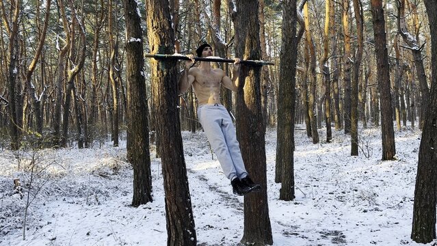 Young sportsman doing static exercises on horizontal bar at forest. Athletic man working out at winter nature. Sportive guy training outdoor. Concept of sport and active lifestyle. Slow motion