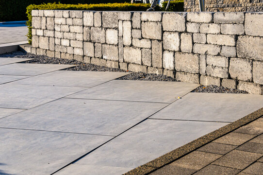 Modern patio with grey concrete paving slabs, gravel accents, and stone retaining wall
