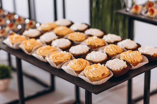 Assortment of Sweet Delights: A delectable spread of mini cupcakes and tartlets, artfully arranged on a dark tray, offers a tempting selection of bite-sized desserts.