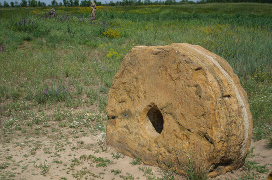 An ancient millstone with a hole in the center against the background of a green field and grass.