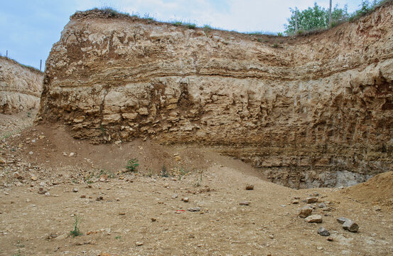 High cliff and quarry with exposure of layered rocks and sand