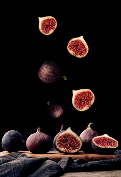 Ripe whole and sliced figs flying over a wooden board on a black background
