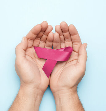 Male hands holding a pink ribbon, symbol of breast cancer awareness